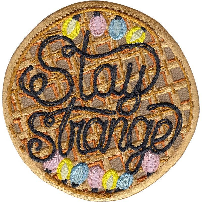 STAY STRANGE Strygemærke, en vaffel med sirup, farver og teksten STAY STRANGE