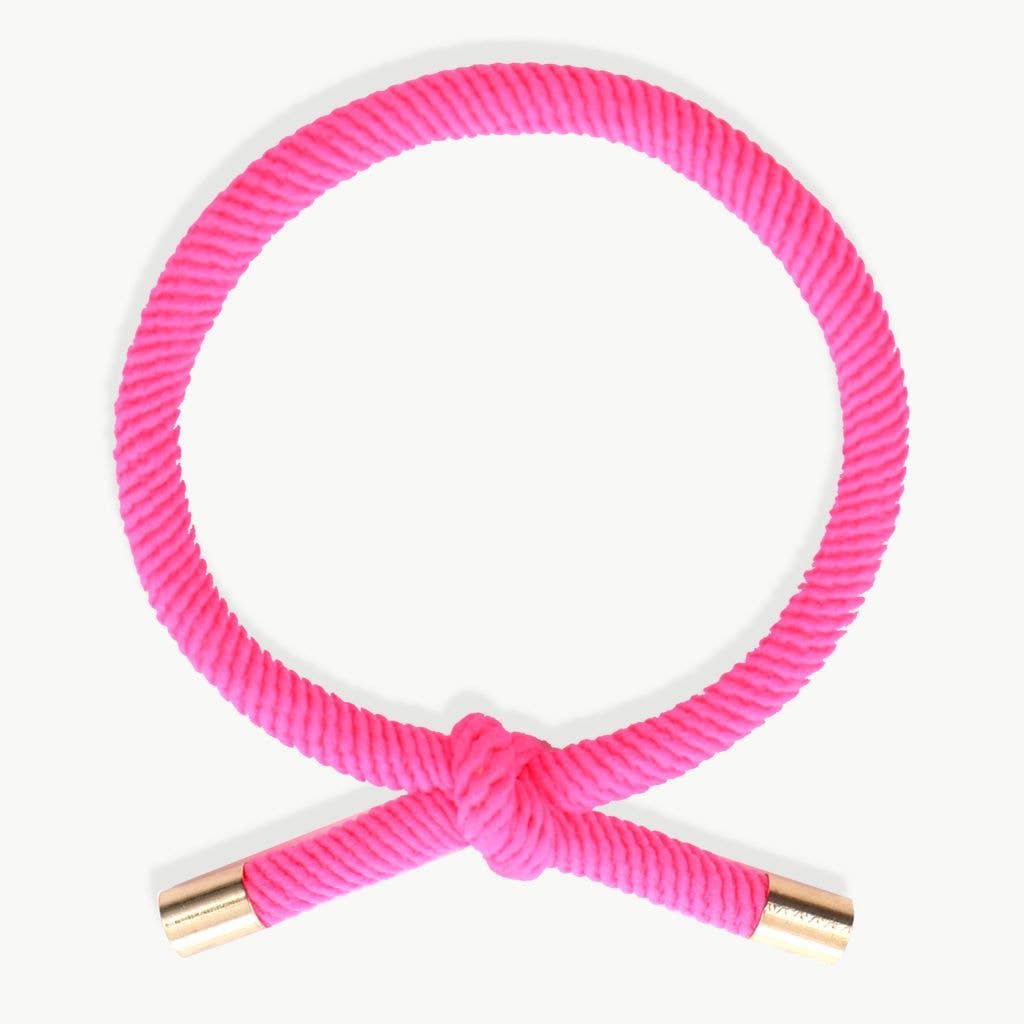 FUCHSIA Hårelastik og armbånd båret på et håndled med synlig knude og guldfarvede endestykker.