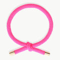 FUCHSIA Hårelastik og armbånd med dekorativ knude og guldfarvede endestykker på lys baggrund.