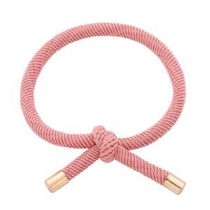 GAMMELROSA Hårelastik og armbånd båret på et håndled med synlig knude og guldfarvede endestykker.