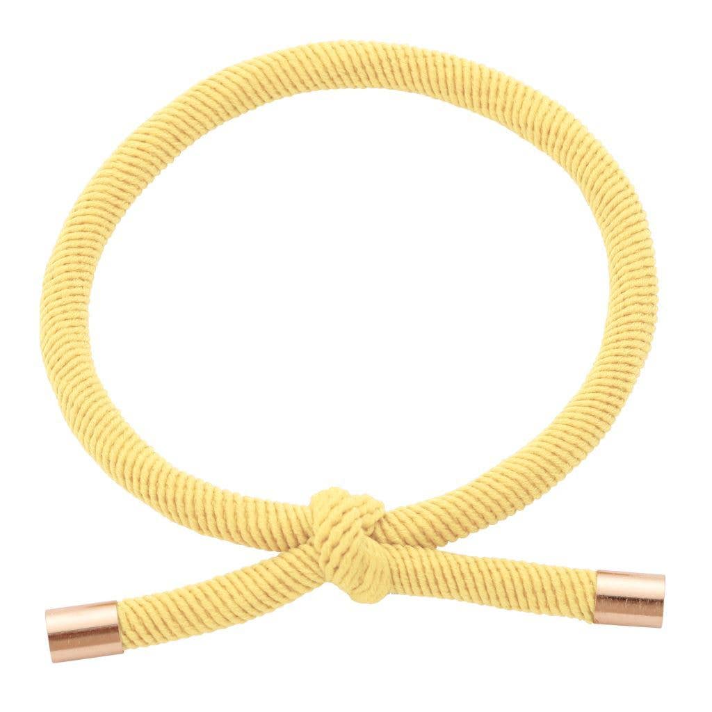 GUL Hårelastik og armbånd med dekorativ knude og guldfarvede endestykker på lys baggrund.