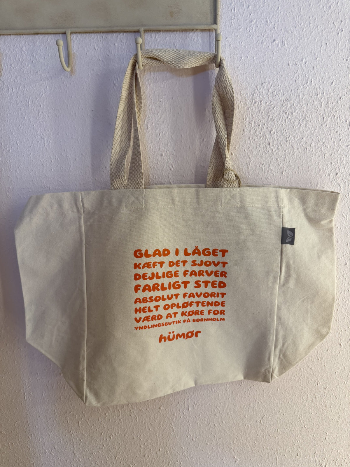HÜMØR naturfarvet totebag med orange teksttryk, vist hængende