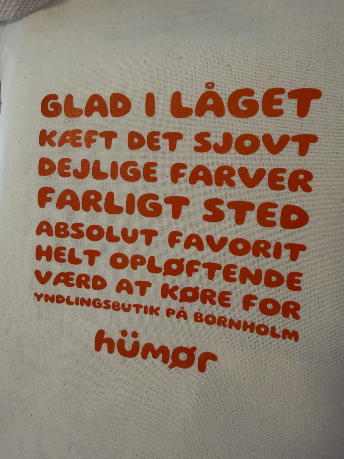 Nærbillede af orange tekst og hümør logo på naturfarvet totebag
