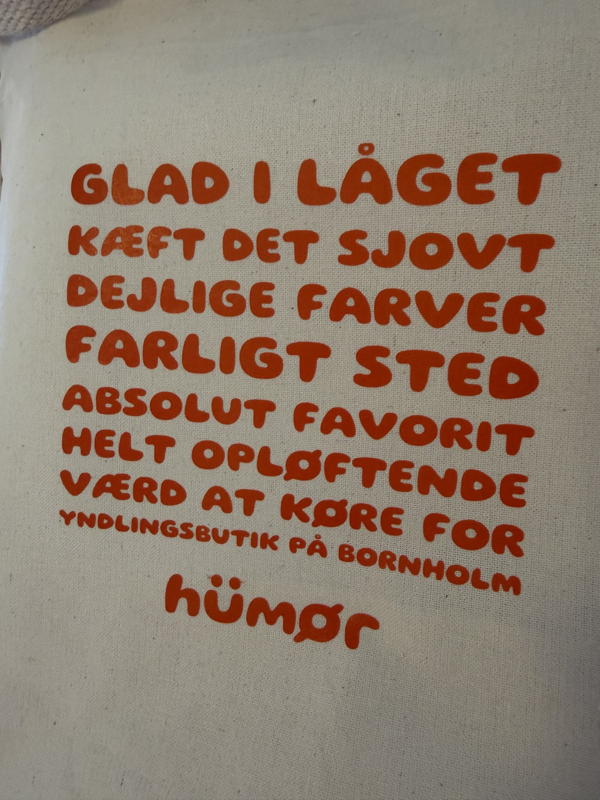 Nærbillede af orange tekst og hümør logo på naturfarvet totebag