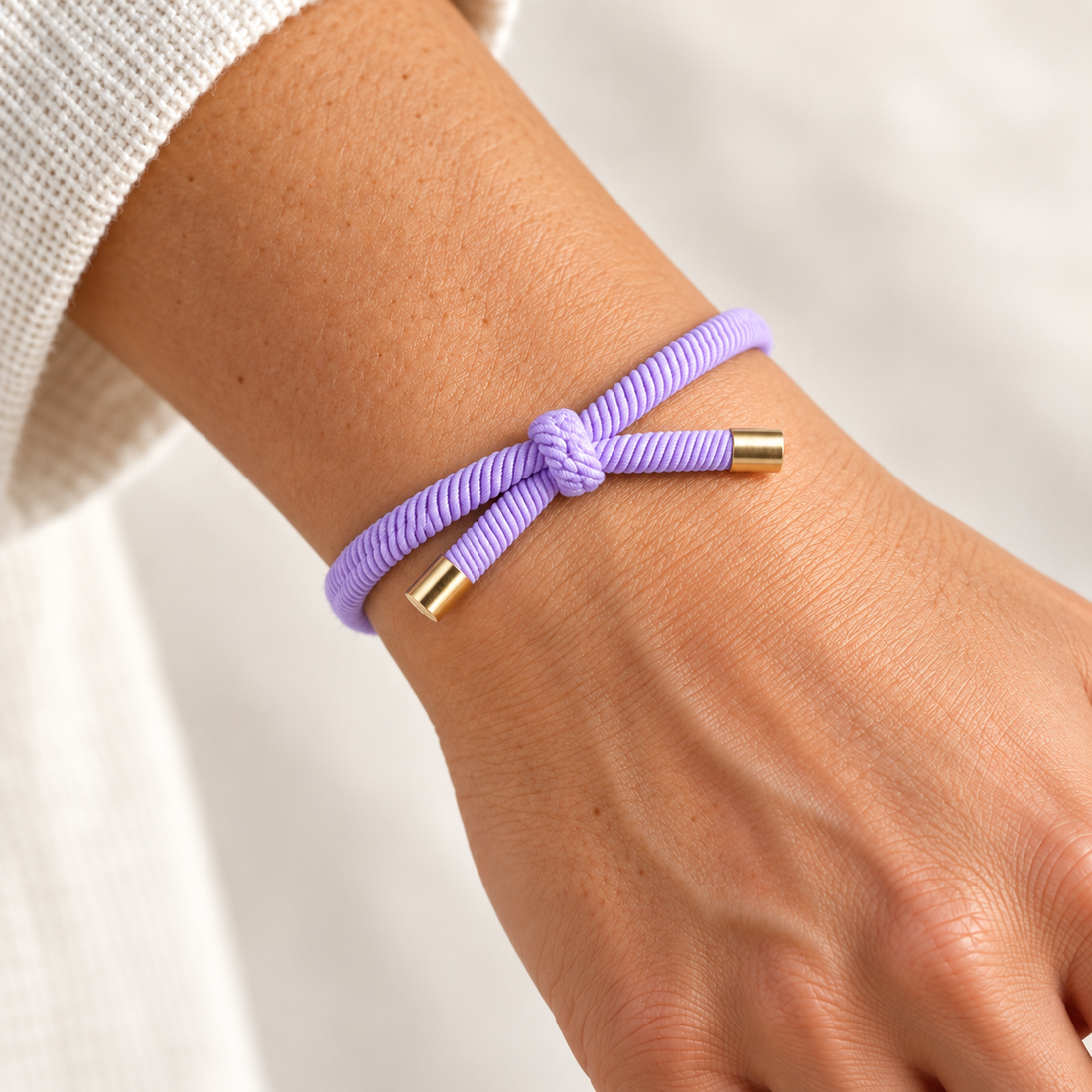 LILLA Hårelastik og armbånd båret på et håndled med synlig knude og guldfarvede endestykker.
