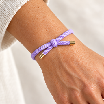 LILLA Hårelastik og armbånd båret på et håndled med synlig knude og guldfarvede endestykker.