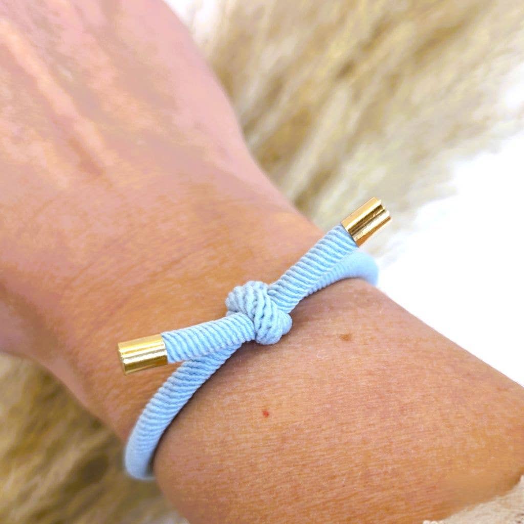 LYSEBLÅ Hårelastik og armbånd med knude og guldfarvede endestykker båret om håndleddet.