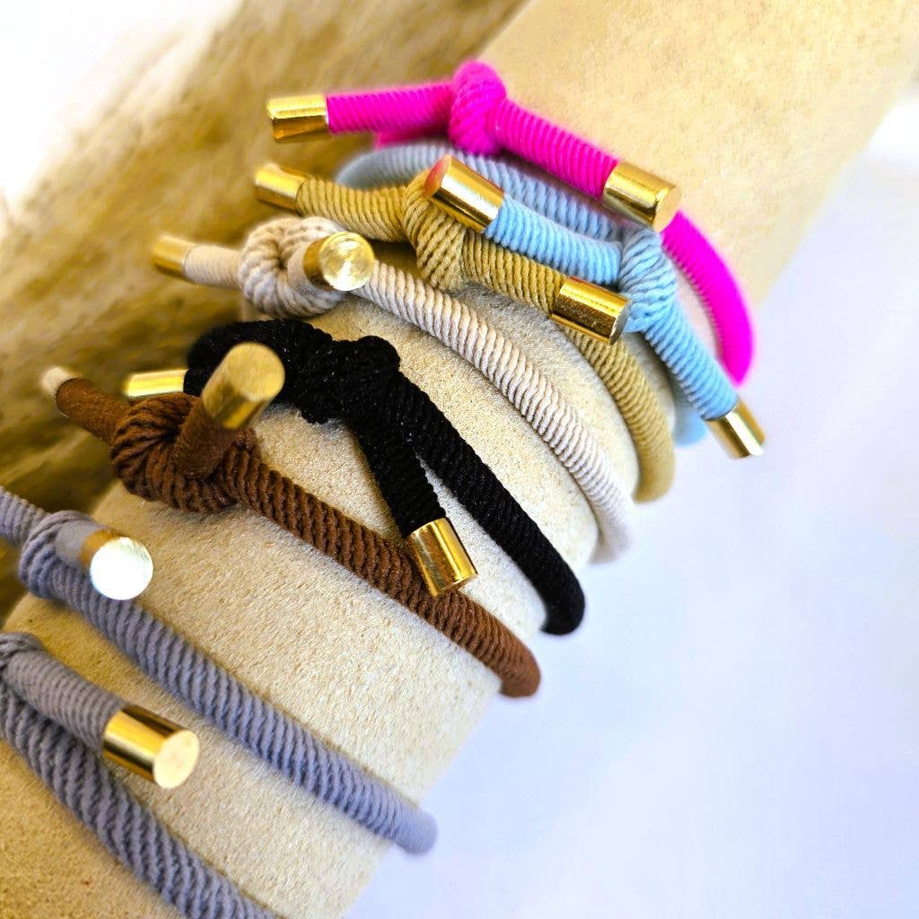 Hårelastikker i flere farver med guldfarvede endestykker båret sammen som armbånd.