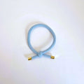 LYSEBLÅ Hårelastik og armbånd med knude og guldfarvede endestykker på lys baggrund.
