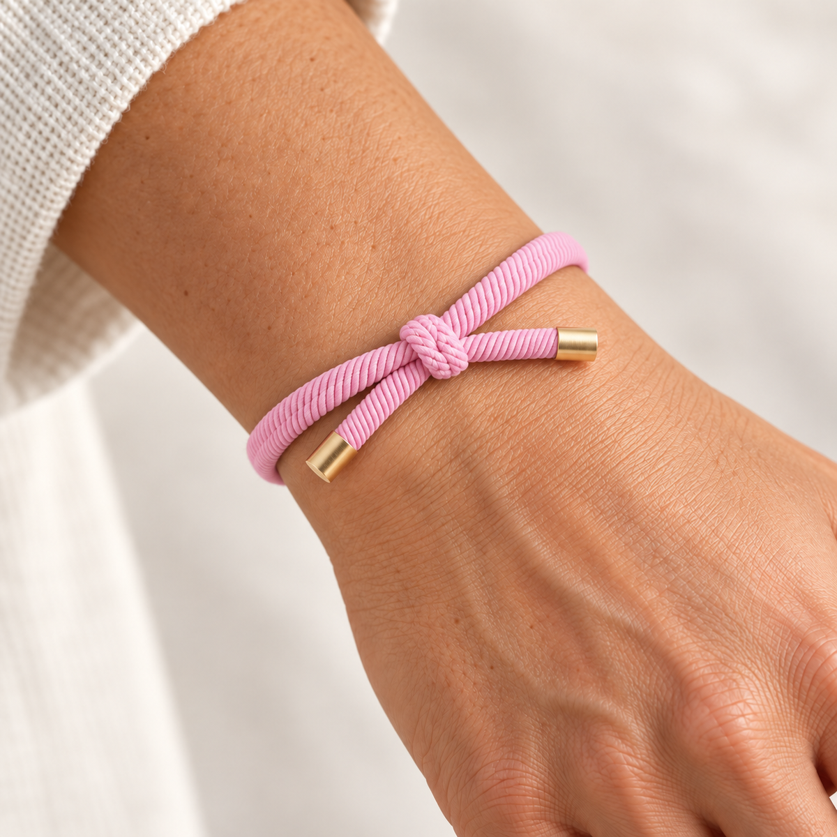 LYSERØD Hårelastik og armbånd båret på et håndled med synlig knude og guldfarvede endestykker.