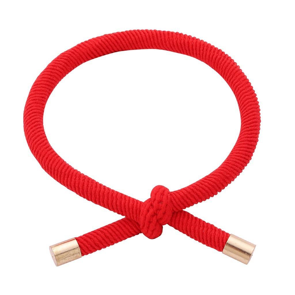 RØD Hårelastik og armbånd båret på et håndled med synlig knude og guldfarvede endestykker.